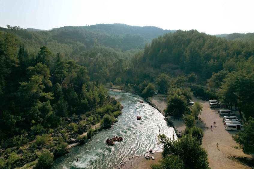 Un río rodeado de un bosque denso, con gente haciendo rafting y un campamento cercano. 1