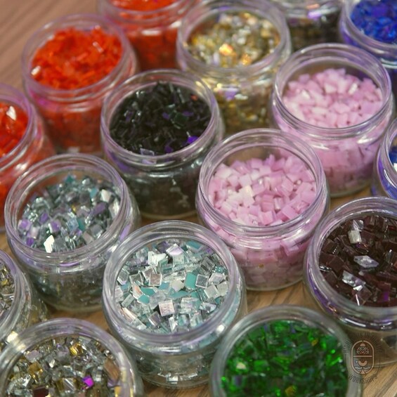 Flera små glasburkar fyllda med olika sorters material i olika färger och med varierande textur, troligen använda för pyssel eller dekoration. 5
