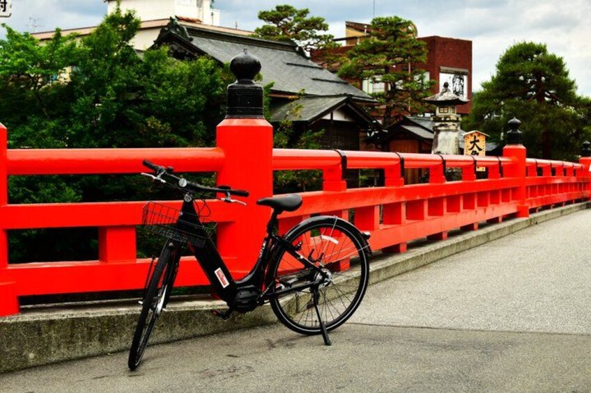 A black bicycle parked on a red bridge with traditional Japanese architecture in the background. 3