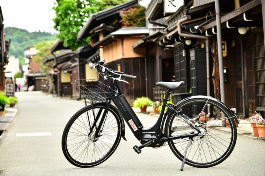 A black bicycle parked on a street with traditional buildings and greenery in the background. 4