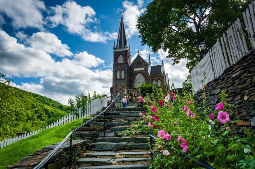 A church with a tall spire, a stone staircase, and pink flowers. 1