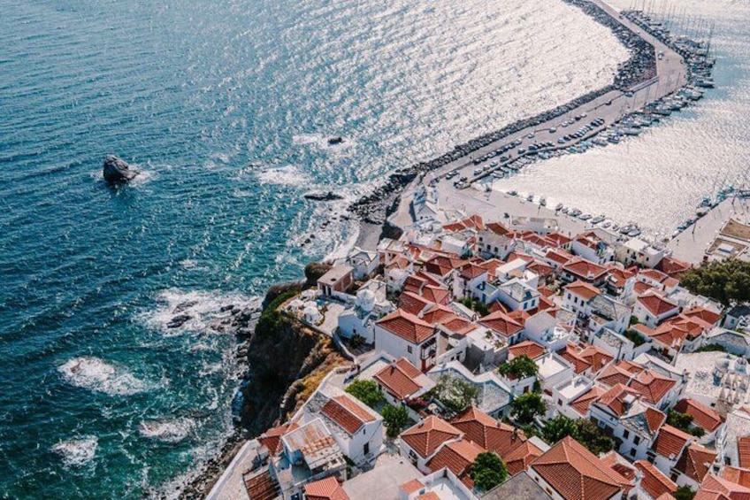 A coastal town with white buildings and red roofs, a beach, and boats in the water. 4