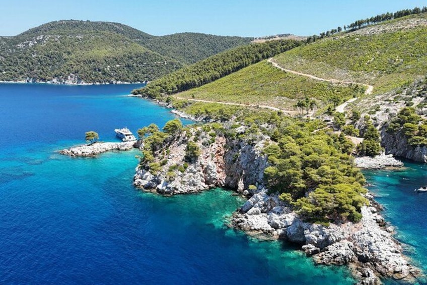 A coastal landscape with clear blue waters, rocky outcrops, and dense green vegetation. 2