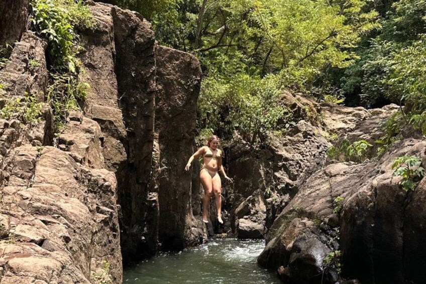 A person jumping into a river surrounded by rocky terrain and greenery. 2