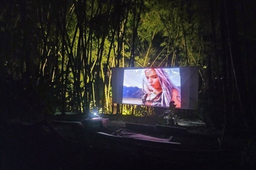 A large outdoor screen displaying a movie scene in a forested area. 1