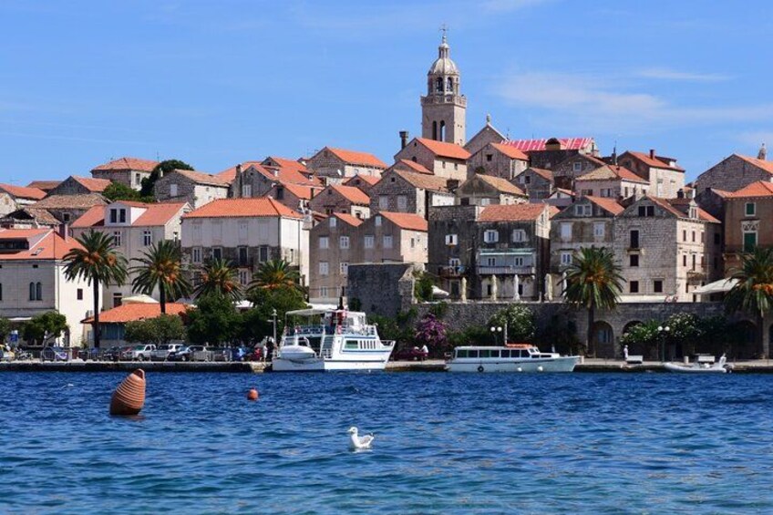 A coastal town with historic buildings, a prominent church tower, and a calm sea with boats. 2