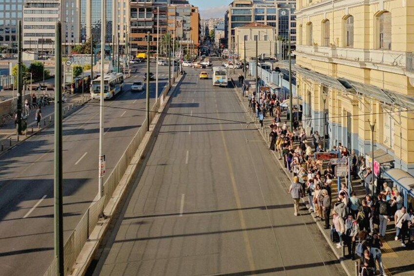 A wide urban street with a crowd of people on the sidewalk, a tram, and tall buildings. 5