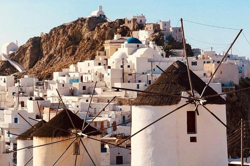 White buildings with blue domes, windmills, and a mountain in the background. 2