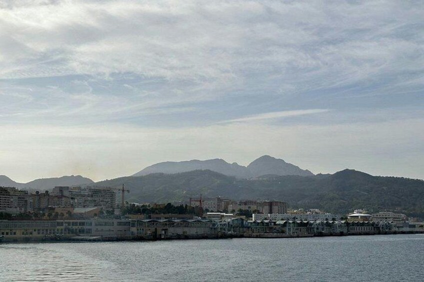A coastal cityscape with buildings, a waterfront, and mountains in the background. 3