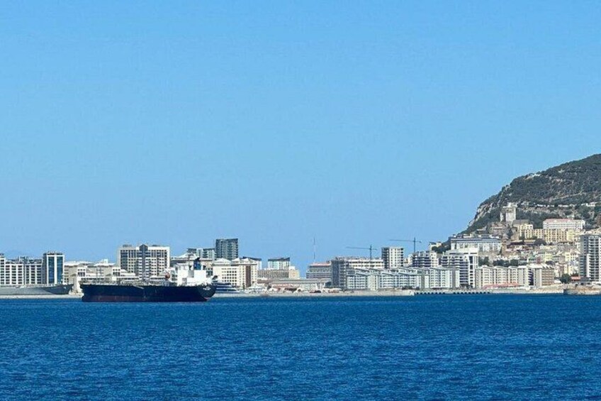 A large ship on the water, a city skyline with buildings, and a hill with vegetation. 5
