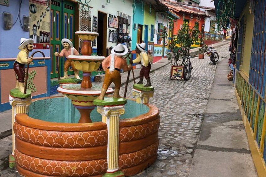 A colorful street with a large fountain sculpture, cobblestone pavement, and buildings with vibrant facades. 5