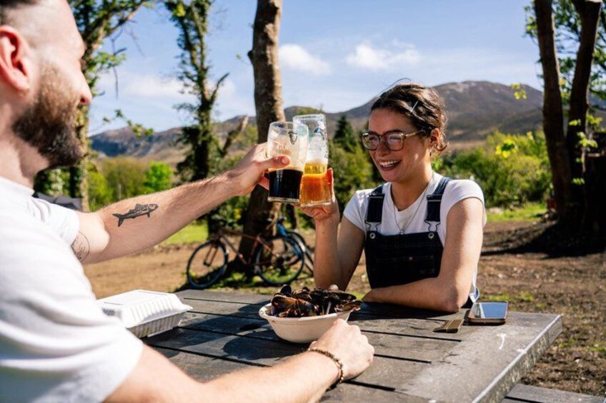Two people toasting with beer glasses, a bicycle, and a scenic outdoor setting with trees and hills in the background. 5