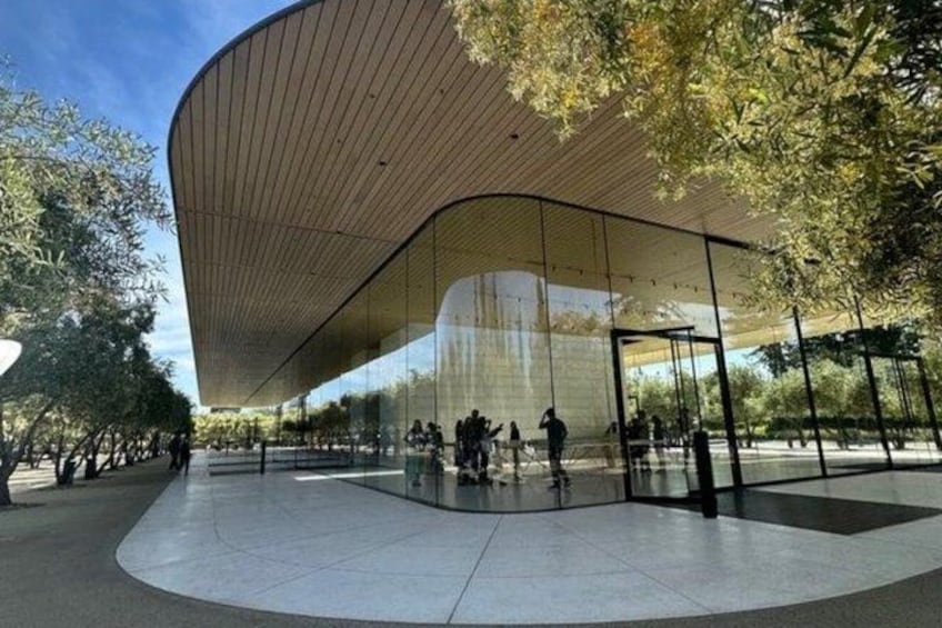 A modern architectural structure with a curved wooden roof and glass walls, surrounded by a spacious plaza with trees. 4