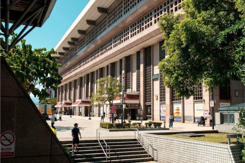 A modern building with large columns, a pedestrian area with steps, and trees. 1