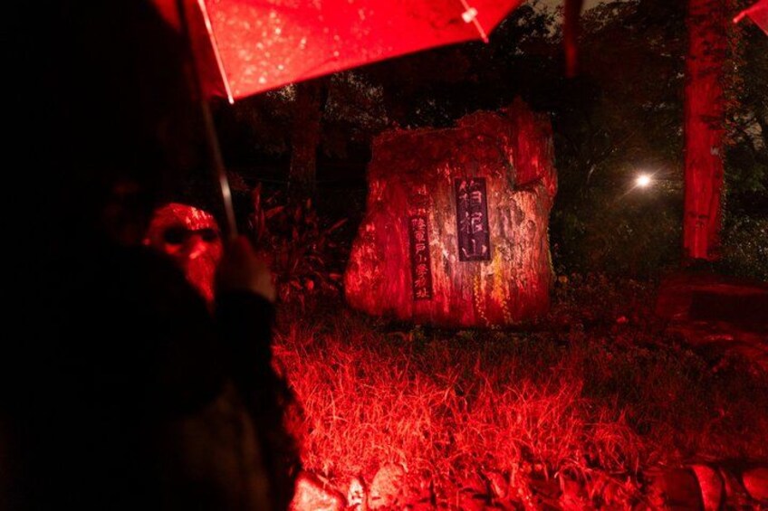 A person holding a red umbrella in a forested area with a large tree stump illuminated by red light. 2