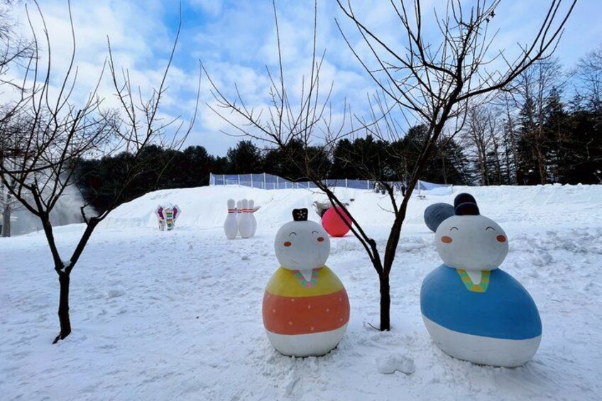 Snow-covered ground with large snowmen sculptures and leafless trees. 4