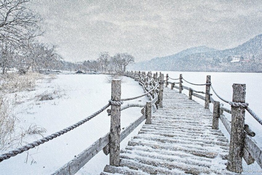A wooden bridge with rope railings leading to a snowy landscape. 3