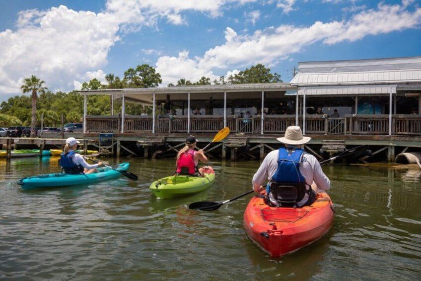 Three kayaks on calm water with a dock and buildings in the background. 1