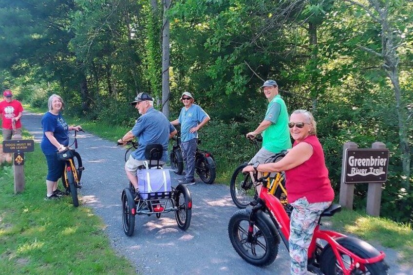 A group of people on bicycles and a wheelchair on a paved path with greenery on both sides. 4
