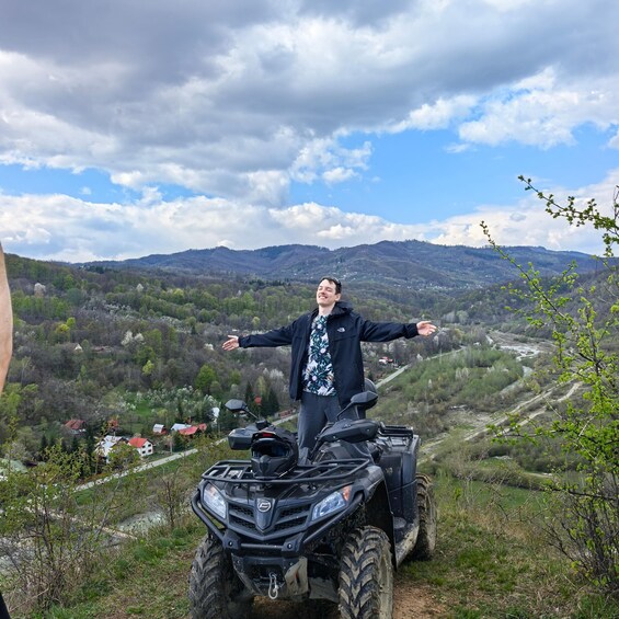 Una persona en un cuatrimoto con los brazos extendidos, observando un valle con casas y montañas al fondo. 2