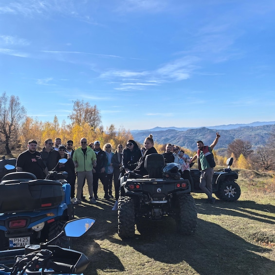 Un grupo de personas en una colina con cuatrimotos, árboles otoñales y una cadena montañosa al fondo. 4