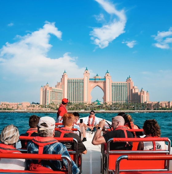 A boat tour with passengers facing a large, pink, multi-towered building in the background. 1