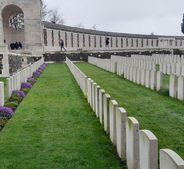 A cemetery with rows of white headstones and a stone archway. 5