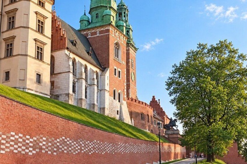 A historic building with a clock tower, a brick wall with a patterned design, and a tree. 4