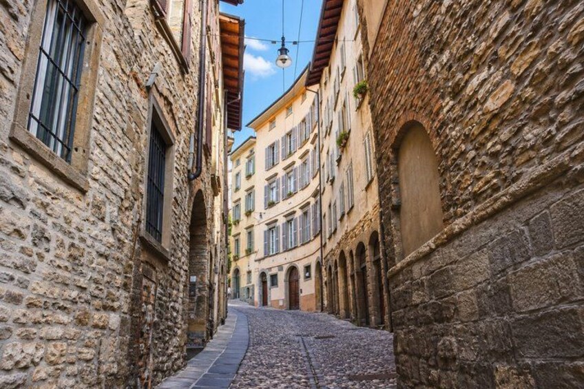 A cobblestone street flanked by historic stone buildings with arched windows and balconies. 5