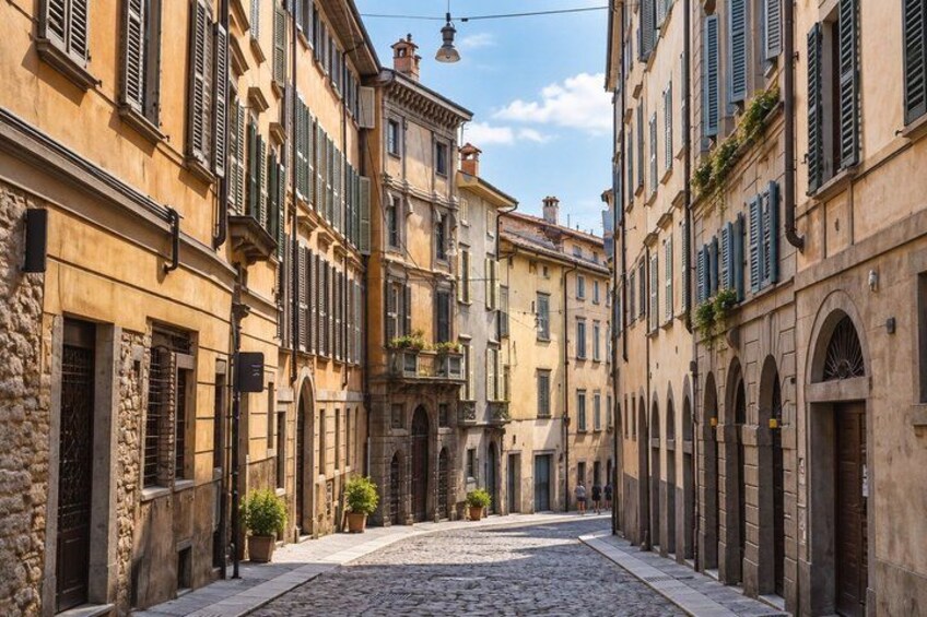 A cobblestone street lined with historic buildings, featuring arched windows and shutters. 2