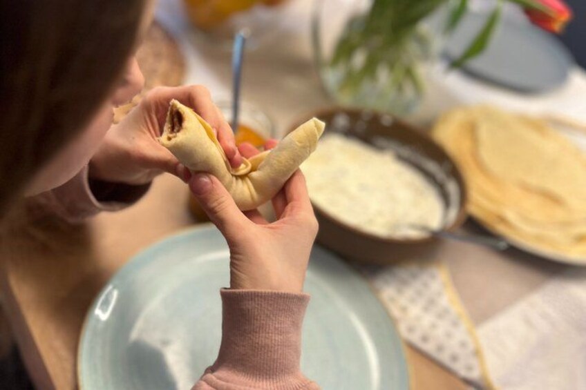 A person holding a wrapped food item, possibly a burrito, with a bowl of sauce and flatbreads in the background. 4