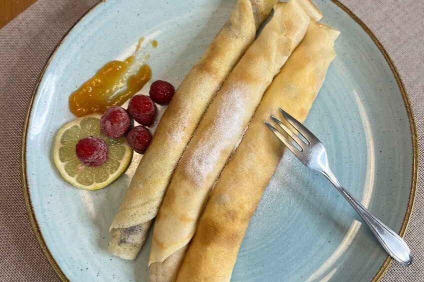 A plate with three rolled pancakes, a slice of lemon, and some raspberries. 2