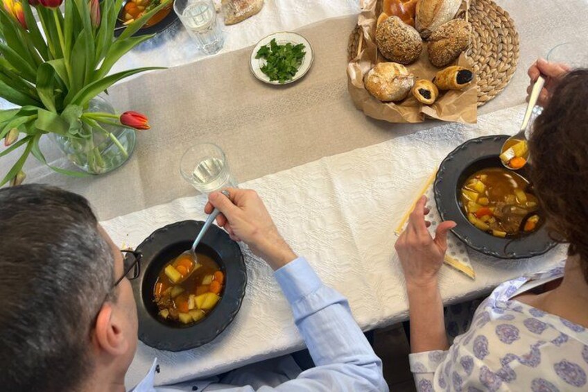 Two people dining at a table with bowls of soup, bread, and a vase of tulips. 5