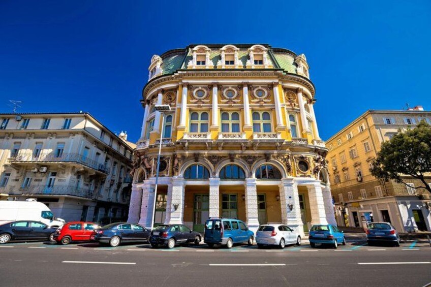 A historic building with ornate architecture, parked cars, and other buildings in the background. 5
