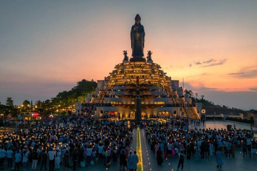A large gathering of people around a multi-tiered monument at sunset. 4