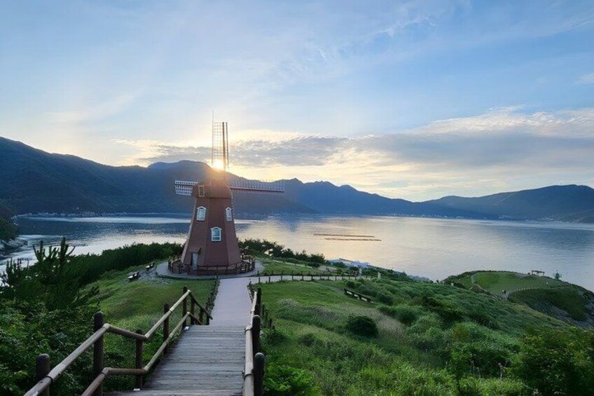 A traditional windmill on a grassy hill overlooking a calm lake with mountains in the background. 3