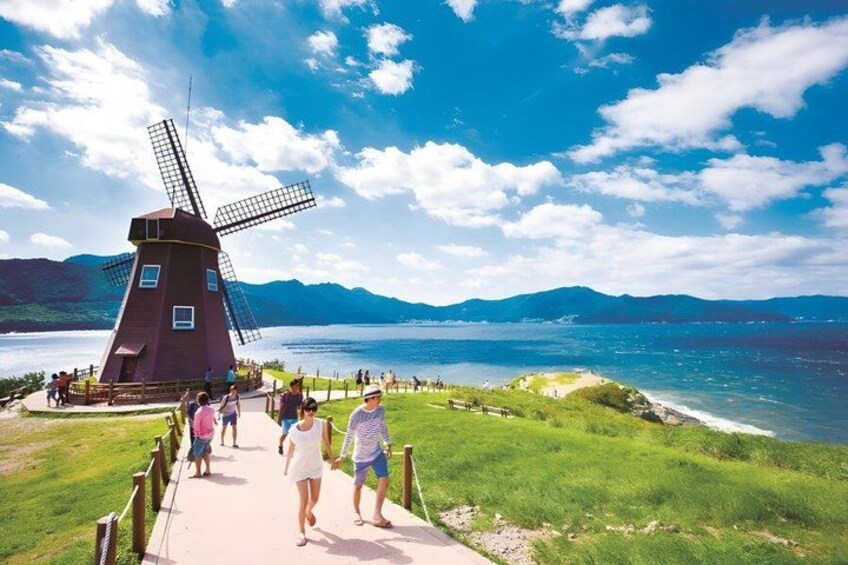 A windmill, a pathway, and a body of water with mountains in the background. 5
