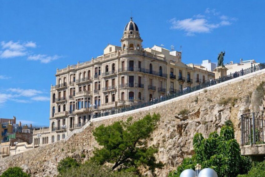 A historic building with a dome, situated on a hillside with a statue and a staircase. 2