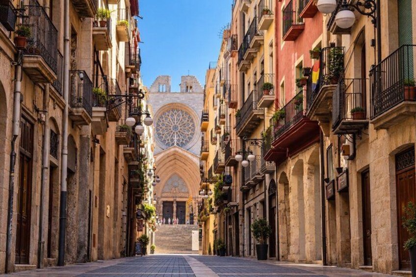 A narrow street flanked by historic buildings with ornate facades and a large cathedral with a rose window in the background. 3