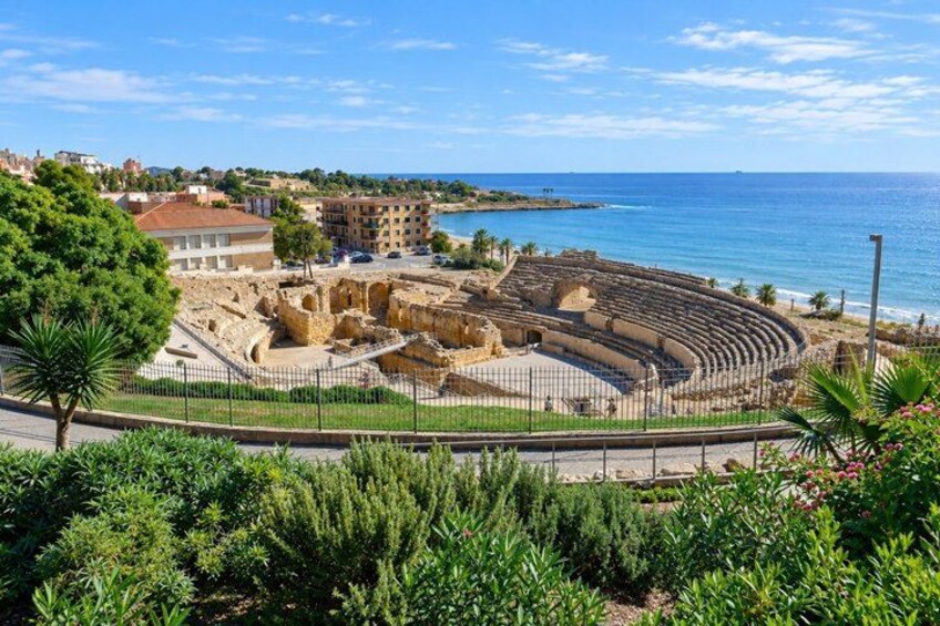 An ancient amphitheater with a clear view of the sea and modern buildings in the background. 5