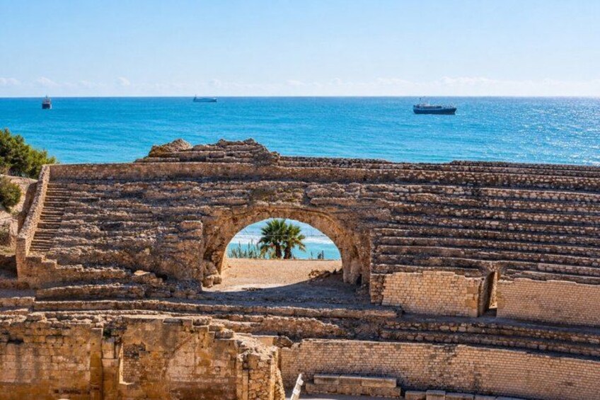 An ancient stone archway leading to a beach with palm trees and the sea in the background. 4