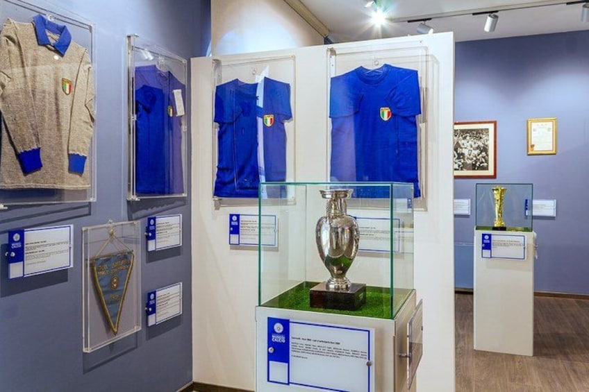 A museum exhibit with sports jerseys, a trophy, and informational plaques. 4