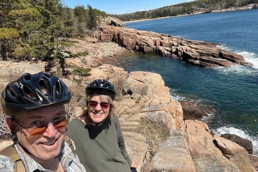 Two people on a rocky shoreline with a body of water and trees in the background. 5