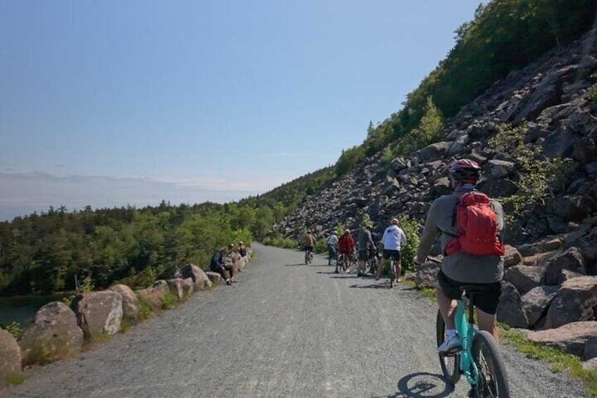 A group of cyclists on a paved road surrounded by rocky terrain and greenery. 3