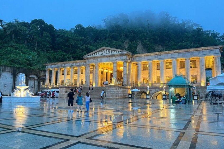 A classical building with columns, a fountain, and people walking around. 1