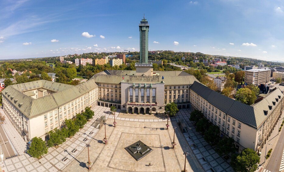 A large square with a central building featuring a tall tower, surrounded by smaller buildings and greenery. 2