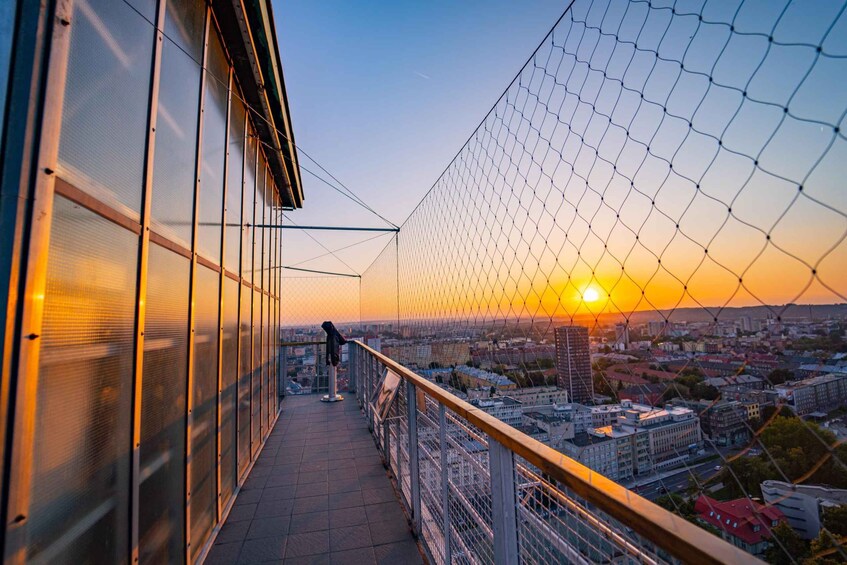 A sunset view from a balcony with a chain-link fence, overlooking a cityscape. 3