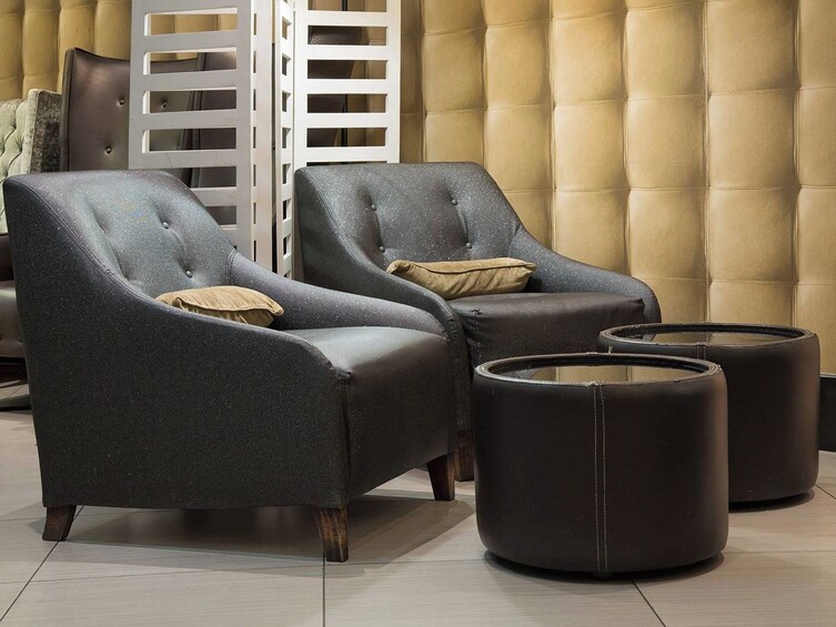 Two dark grey armchairs with wooden legs and beige cushions, placed in front of a tufted beige sofa. 2