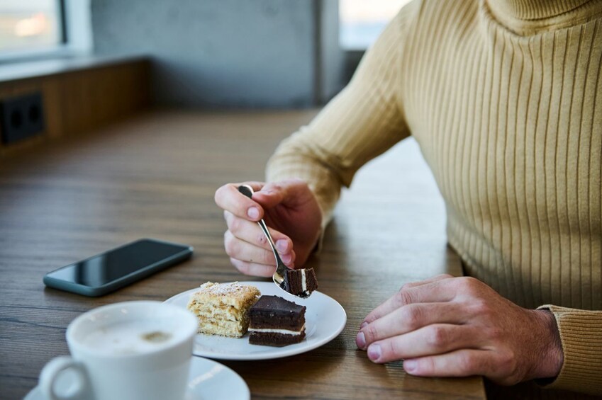 A person eating a slice of cake with a fork, a cup of coffee, and a smartphone on a table. 5
