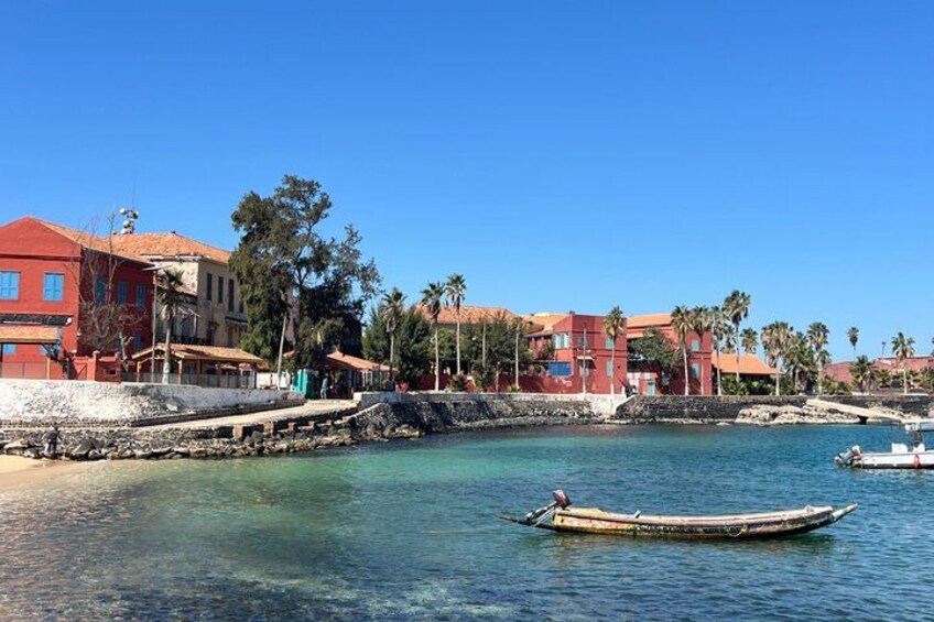 A coastal town with buildings, a clear blue sea, and a wooden boat. 1